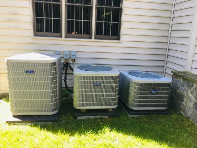 Three outdoor residential Carrier air conditioning condenser units installed beside a home for central cooling and HVAC climate control.