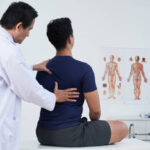 Doctor checking spine of a young man within the annual medical examination
