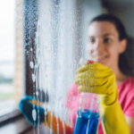 Young woman wiping windows at home