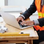 imgi_8_unrecognizable-man-neon-safety-vest-business-suit-sitting-desk-using-laptop_1098-17504