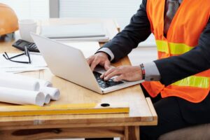 imgi_8_unrecognizable-man-neon-safety-vest-business-suit-sitting-desk-using-laptop_1098-17504