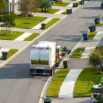 Garbage truck picking up trash bins on suburban street side.